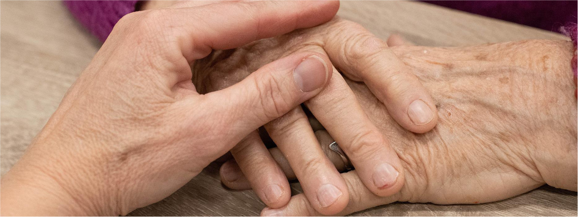 Zbliżenie na dłonie dwóch osób. Dłoń młodej osoby położona jest na dłoni starszej osoby.