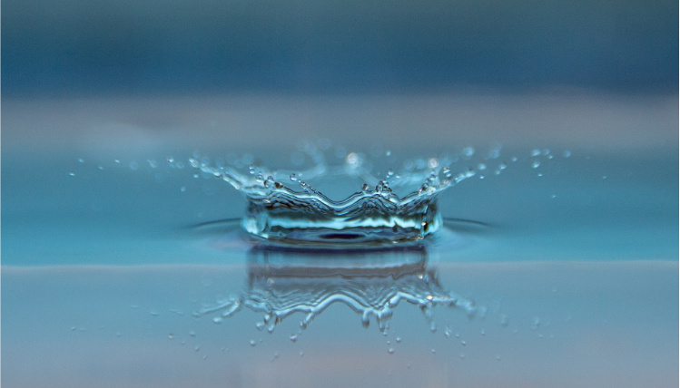 Zdjęcie ilustracyjne. Kropla wody rozpryskuje się o płaską powierzchnię wody.