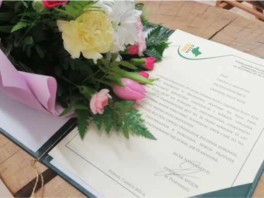 List gratulacyjny od dyrektora WODR, Jacka Sommerfelda. Obok leży bukiet kwiatów.