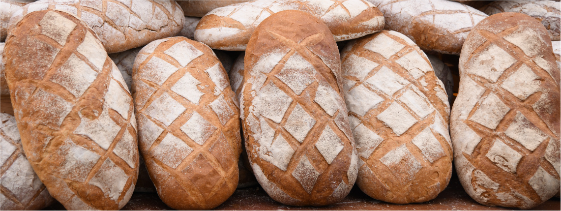 Zbliżenie na ułożone obok siebie bochenki chleba posypane mąką.
