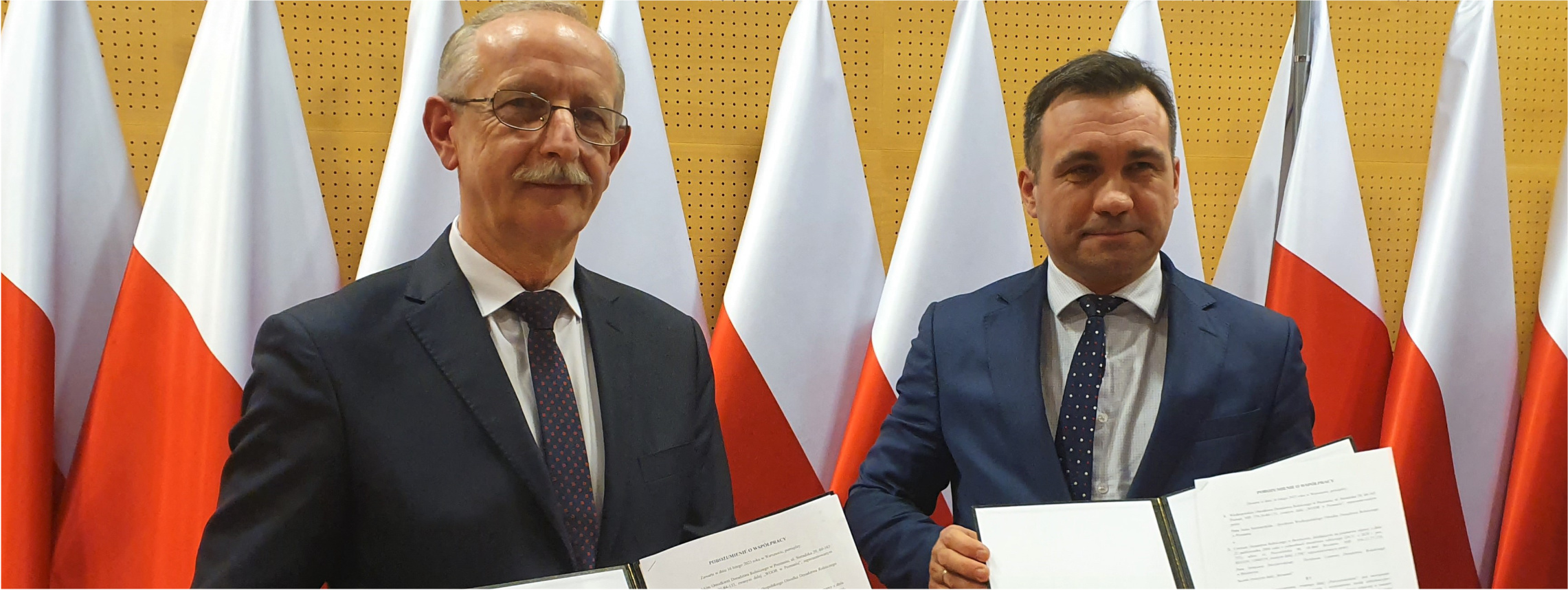Jacek Sommerfeld (z prawej) oraz Ireneusz Drozdowski (z lewej) pozują do zdjęcia trzymając podpisane porozumienia o współpracy.