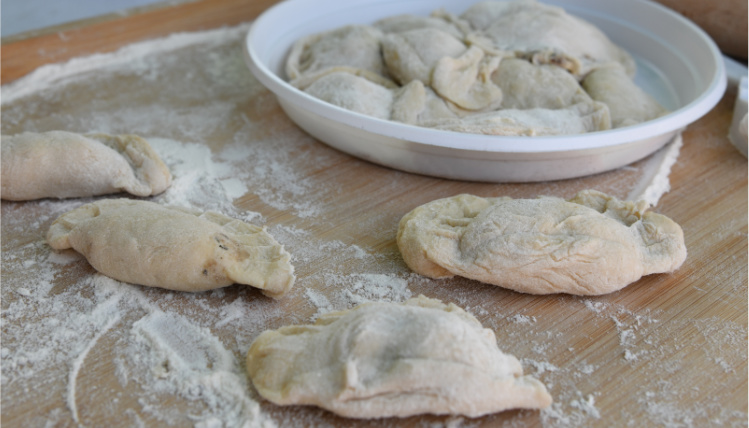 Zbliżenie na drewnianą deskę, na której leżą ulepione pierogi poprószone mąką.