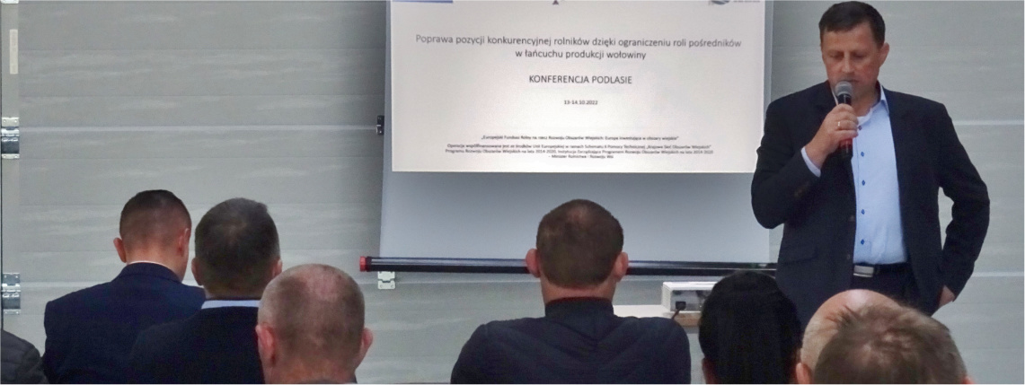 Sprawozdanie z projektu: „Poprawa pozycji konkurencyjnej rolników dzięki ograniczeniu roli pośredników w łańcuchu produkcji wołowiny” Mężczyzna przemawia przez mikrofon, za jego plecami jest ekran z wyświetloną prezentacją. Przed nim siedzą słuchacze widziani od tyłu.