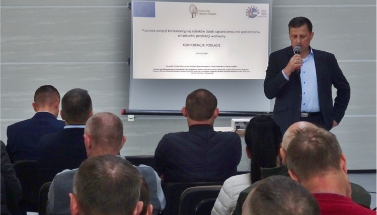 Sprawozdanie z projektu: „Poprawa pozycji konkurencyjnej rolników dzięki ograniczeniu roli pośredników w łańcuchu produkcji wołowiny” Mężczyzna przemawia przez mikrofon, za jego plecami jest ekran z wyświetloną prezentacją. Przed nim siedzą słuchacze widziani od tyłu.