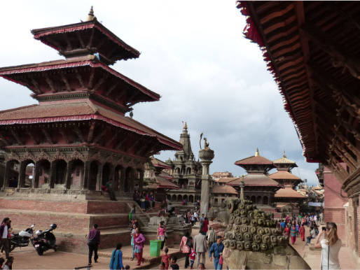 Miejski plac w Nepalu. Między charakterystycznymi azjatyckimi budynkami przechadzają się mieszkańcy. 