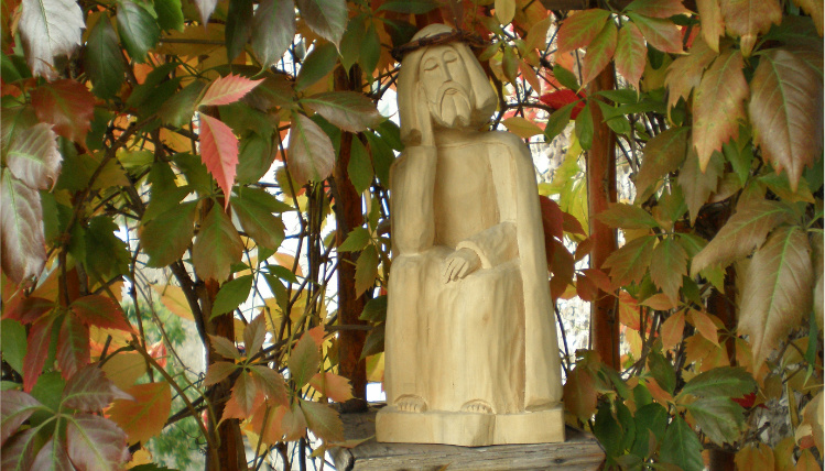 Na postumencie znajduje się drewniana figurka przedstawiająca postać siedzącego Jezusa. Otaczają ją liście.