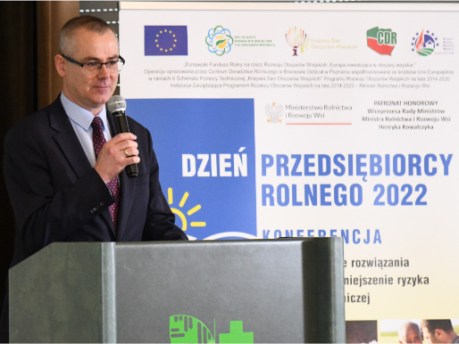 Mężczyzna stoi przy mównicy i przemawia przez mikrofon. Obok niego jest baner z hasłem Dzień Przedsiębiorcy Rolnego 2022.