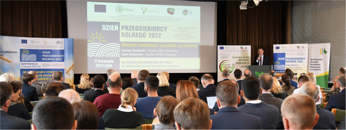 Nowoczesne rozwiązania hasłem Dnia Przedsiębiorcy Rolnego 2022 Grupa ludzi siedzi w sali, widziani są od tyłu. Przed nimi jest ekran z wyświetloną prezentacją. Obok stoi mężczyzna, który przemawia przez mikrofon.
