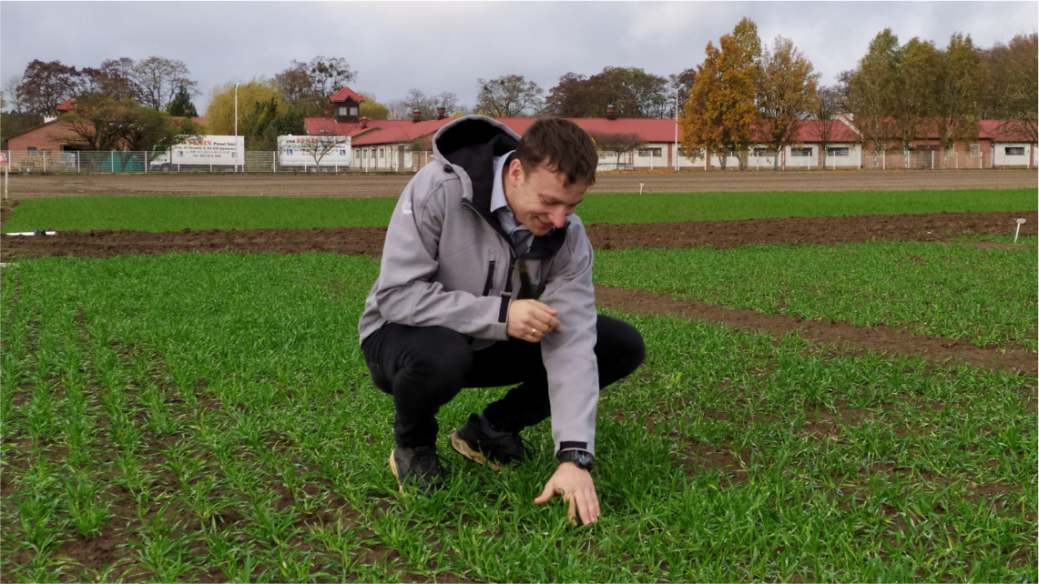 Zdobywca drugiego miejsca w konkursie, Łukasz Kuleczka kuca na polu i dotyka ręką ziemi.