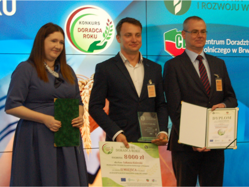 Łukasz Kuleczka prezentuje nagrodę za zdobycie drugie miejsca. Obok stoi wiceminister rolnictwa Anna Gembicka i wicedyrektor WODR Maciej Szłykowicz.