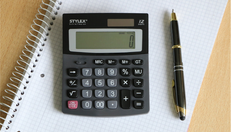 Ujęcie od góry na kalkulator oraz długopis, które leżą na otwartym zeszycie w kratkę.