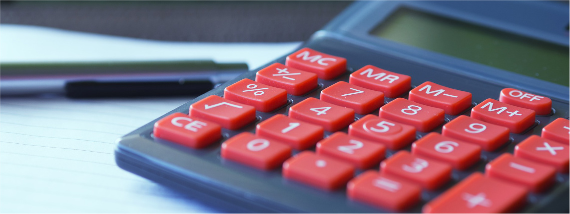 Zbliżenie na kalkulator z czerwonymi klawiszami. Obok leży długopis.