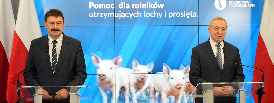 Dwaj mężczyźni w średnim wieku (z prawej Henryk Kowalczyk, z lewej Ryszard Bartosik) stoją przed mównicami. Za nimi jest flaga Polski oraz zdjęcie trzody chlewnej. 