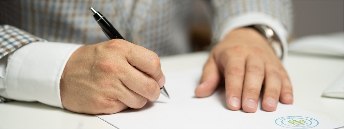 Grafika ilustracyjna. Na zbliżeniu widać ręce mężczyzny, który podpisuje prawą dłonią dokumenty.