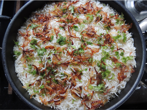 Zbliżenie na patelnię z gotującą się potrawą z kuchni azjatyckiej. Widać ryż oraz warzywa.