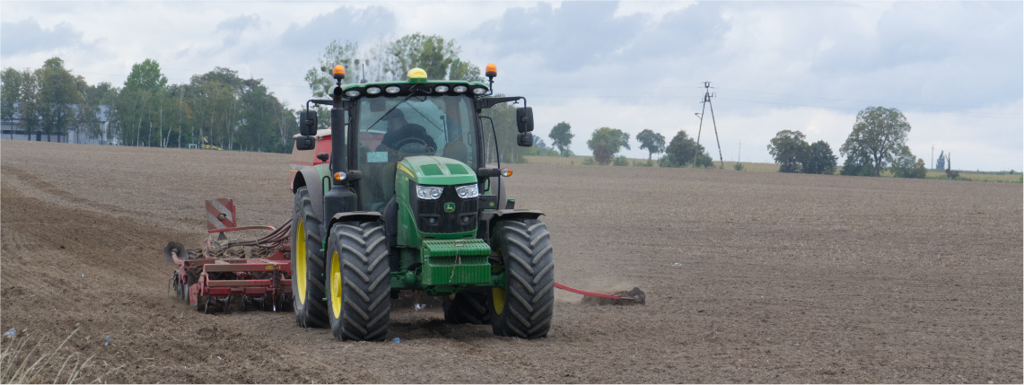 Systemy uprawy roli z wyszczególnieniem technologii strip-till Po polu jedzie zielony ciągnik z doczepioną maszyną do pracy w polu. Ciągnik jest widoczny od przodu. W tle na horyzoncie widać drzewa.