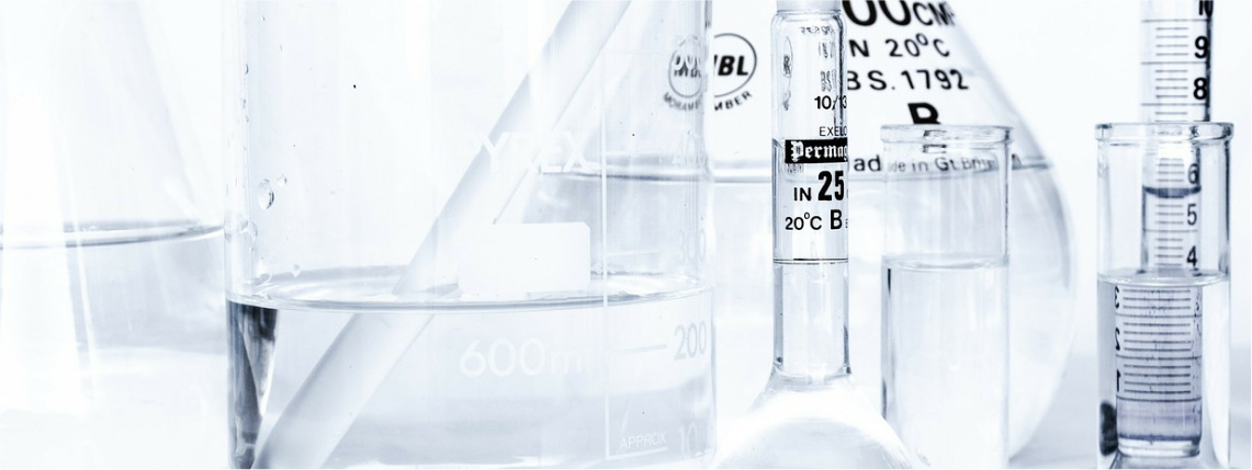 Przezroczyste zlewki i fiolki chemiczne stoją obok siebie. Mają napisy określające pojemność.