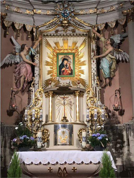 Ołtarz w kościele. W centrum znajduje się obraz z wizerunkiem Matki Bożej. Dookoła są zdobione rzeźby aniołów oraz złote elementy. 