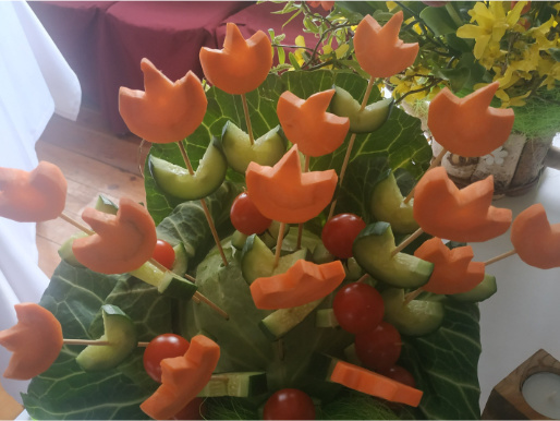 Na stole stoi widoczna z bliska ozdoba przypominająca kwiaty wykonana z warzyw.