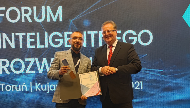 Maciej Zacharczuk, kierownik projektu eDWIN, odebrał Polską Nagrodę Inteligentnego Rozwoju, którą otrzymał Wielkopolski Ośrodek Doradztwa Rolniczego w Poznaniu Maciej Zacharczuk (po lewej) stoi obok mężczyzny w średnim wieku i trzyma nagrodę z dyplomem. Na niebieskim tle z tyłu jest napis "Forum Inteligentnego Rozwoju".