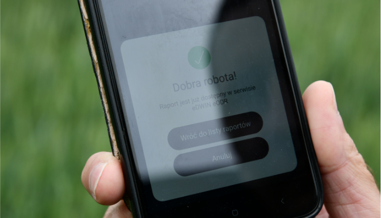 Projekt eDWIN ma pomóc rolnikom w prowadzeniu gospodarstwa Zbliżenie na ekran telefonu, który znajduje się w dłoni. Na ekranie widać panel z napisem "Dobra robota! Raport jest już dostępny w serwisie eDWIN eODR". Poniżej są przyciski "wróć do listy raportów" oraz "anuluj".
