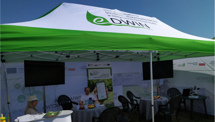 Projekt eDWIN był promowany na Krajowych Dniach Pola w Minikowie w 2021 roku Słoneczny dzień. Namiot z logotypem eDWIN na dachu. W środku są telewizory, doradcy rolniczy, krzesła i stoły.