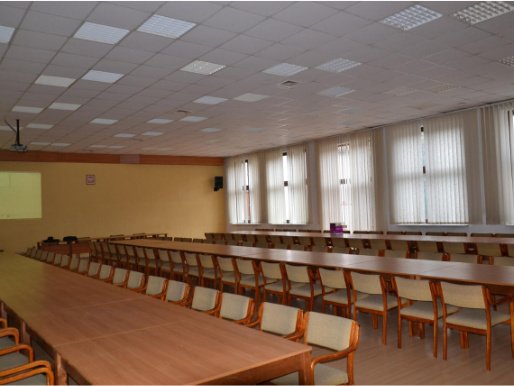 Wnętrze sali konferencyjnej w Sielinku Wnętrze sali konferencyjnej. Drewniane stoły i krzesła stoją w dwóch rzędach. W tle widać okna.