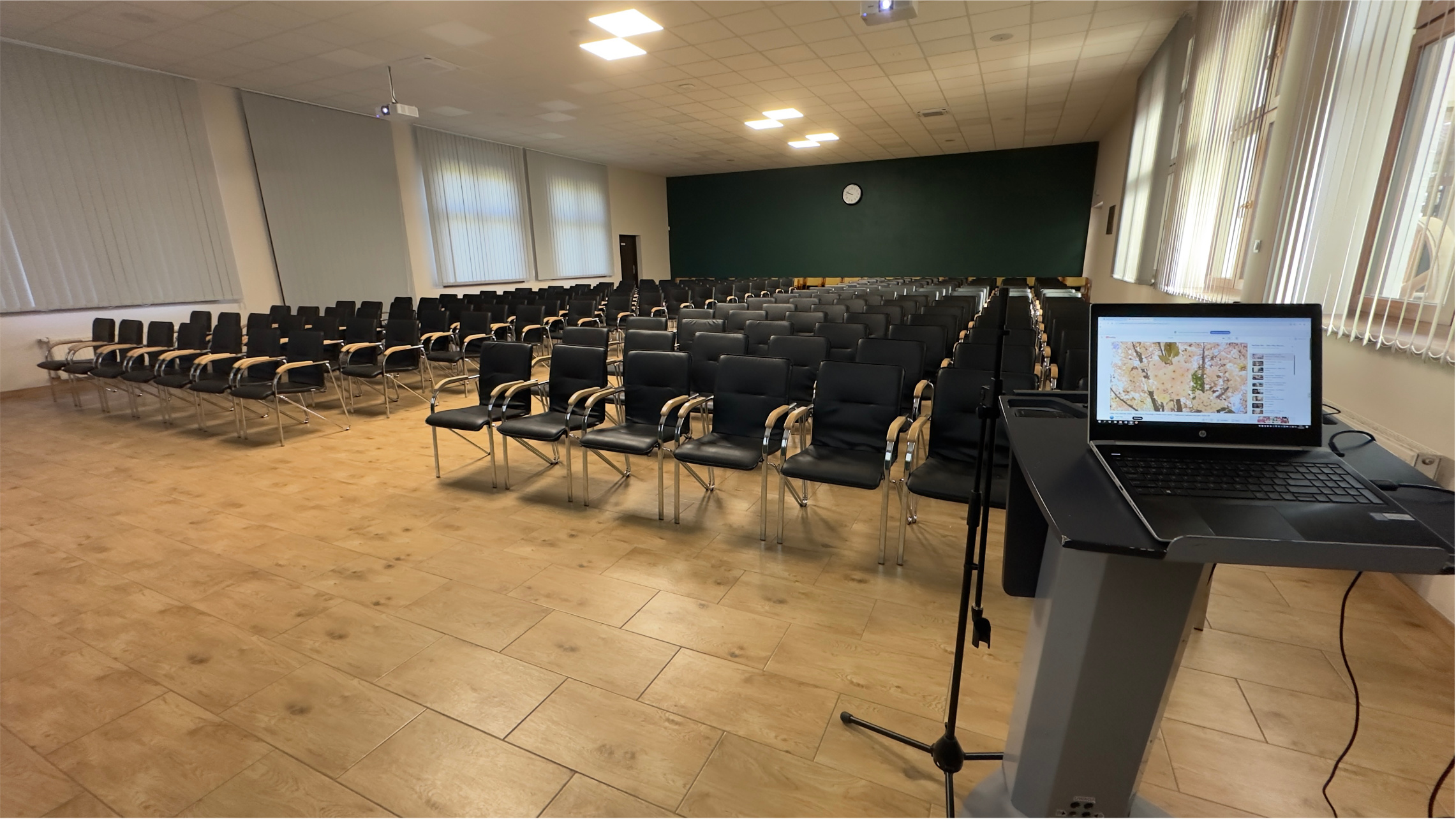 Wnętrze sali konferencyjnej w Sielinku Wnętrze sali konferencyjnej. Drewniane stoły i krzesła stoją w dwóch rzędach. W tle widać okna.