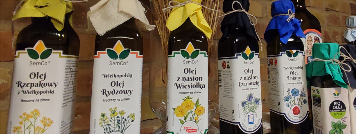 Firma Semco produkuje około 40 różnych rodzajów olei Szklane butelki z olejem stoją na obrusie na półce przed ceglaną szklaną. Na butelkach olejów są etykiety z informacją o rodzajach olei.