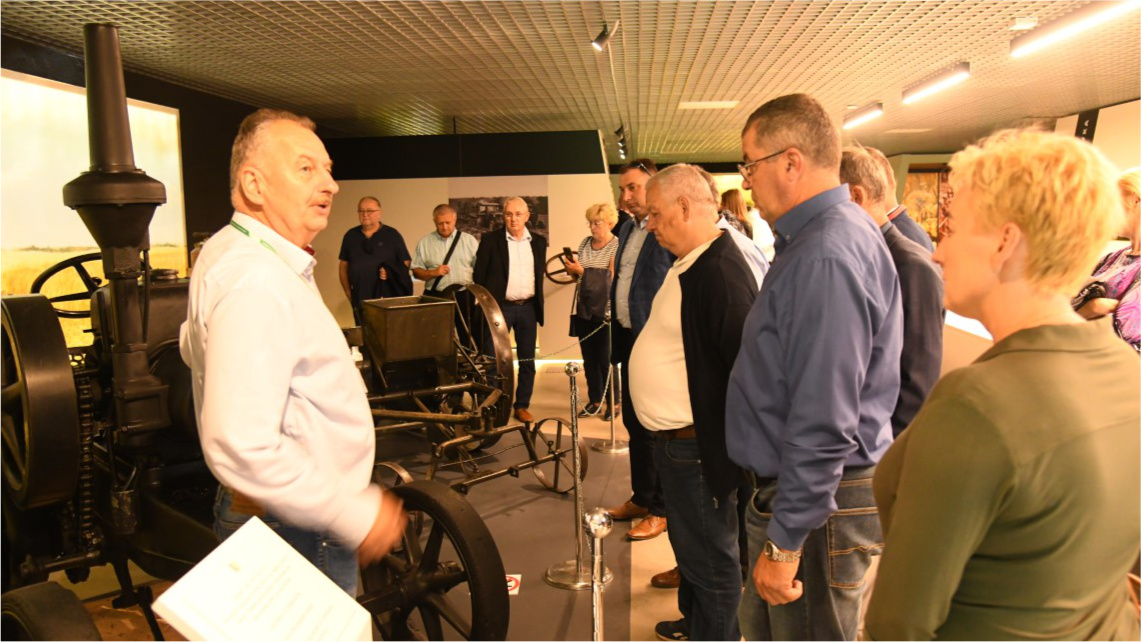 Grupa kilku osób ogląda starą maszynę rolniczą w muzeum w Szreniawie