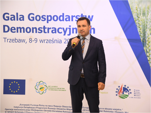 Dyrektor Jacek Sommerfeld podkreślał wielkie znaczenie Sieci Gospodarstw Demonstracyjnych Dyrektor Jacek Sommerfeld przemawia przez mikrofon na tle ścianki reklamowej.
