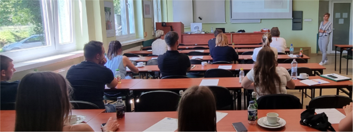 Drugie spotkanie z cyklu szkoleń dotyczących żywienia krów mlecznych Sala lekcyjna. W ławkach siedzą słuchacze, widoczni od tyłu. Przed nimi jest wykładowca, który omawia prezentację wyświetloną z rzutnika na ekranie.