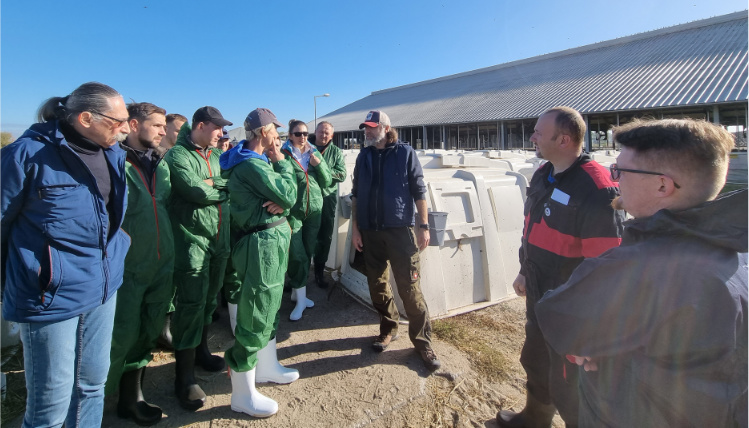 Praktyka czyni mistrza. „Akademia żywienia krów mlecznych – wyzwania współczesnego producenta mleka” Na podwórzu stoi grupa ludzi, zwrócona przodem do mężczyzny, który przemawia.