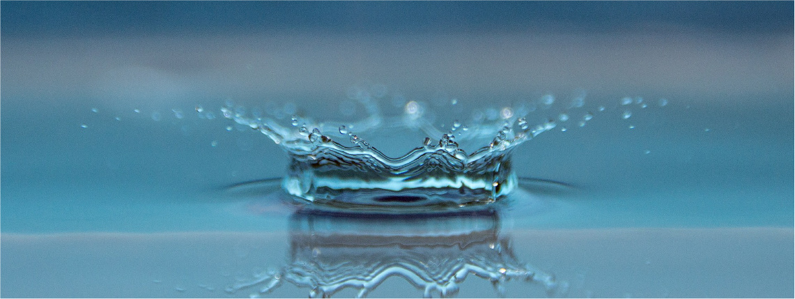Zdjęcie ilustracyjne. Kropla wody rozpryskuje się o płaską powierzchnię wody.