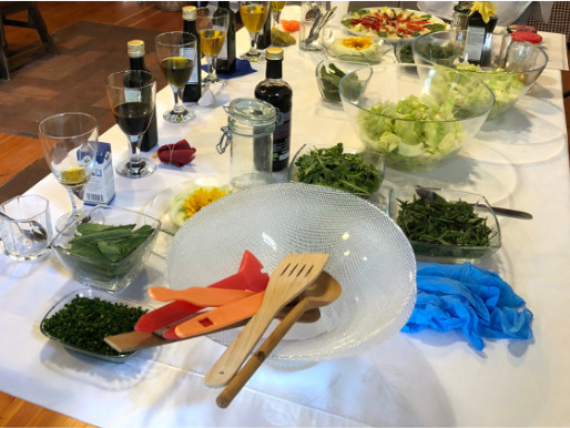 Wnętrze pomieszczenia. Na stole zakrytym obrusem stoją różnorodne naczynia, przystawki oraz oleje.