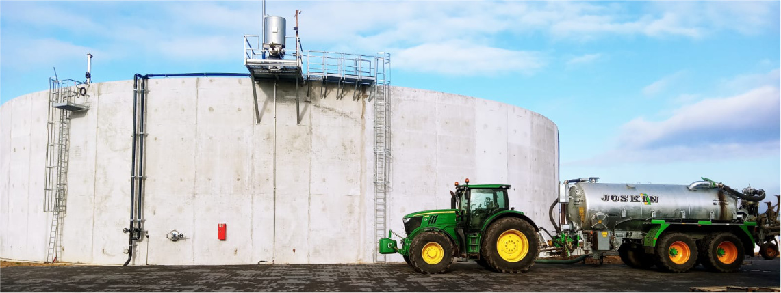 W centralnej części zdjęcia widać betonowy okrągły zbiornik. Obok niego stoi traktor z dołączoną cysterną.