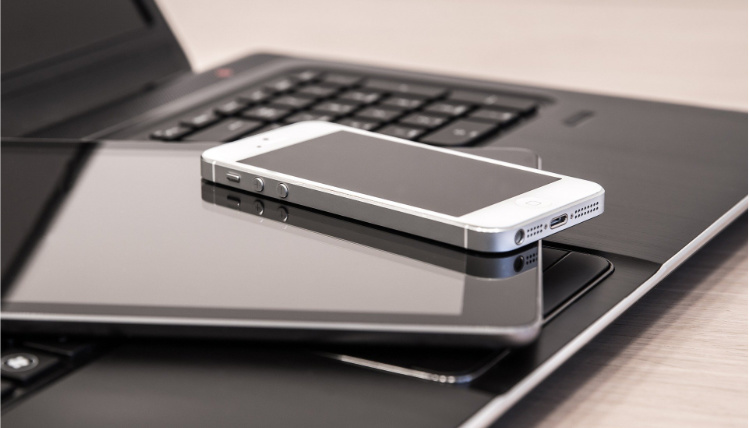 Zdjęcie ilustracyjne - telefon komórkowy i tablet leżą na otwartym laptowie.