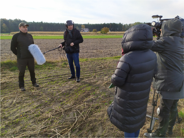 Pochmurny dzień. Ekipa telewizyjna nagrywa wypowiedź Piotra Łukaszewskiego na polu.