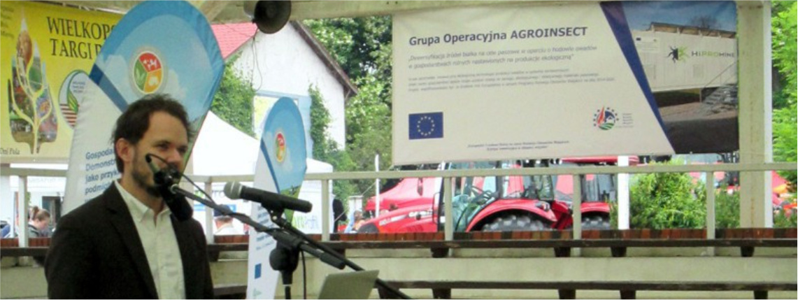 Wnętrze hali. Młody mężczyzna, Krzysztof Dudek, z firmy HiProMine prezentuje na Wielkopolskich Targach Rolniczych w Sielinku projekt grupy AgroInsect.