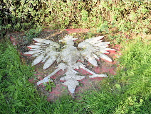 W ziemi na trawniku jest wmurowany kamień z wizerunkiem orła białego, symbolu godła Polski.