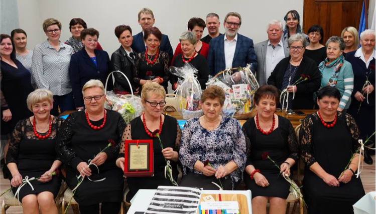 Dwa stowarzyszenia w gminie Brudzew obchodziły jubileusze istnienia W pomieszczeniu znajduje się kilkanaście osób. W pierwszym rzędzie siedzą kobiet z Koła Gospodyń Wiejskich. Jedna z nich trzyma pamiątkową tabliczkę. Na stole znajdują się kosze z prezentami.