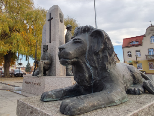 Pomniki na rynku w Margoninie. Na pierwszym planie widać posąg lwa, w tle jest pomnik z sylwetkami żołnierzy.