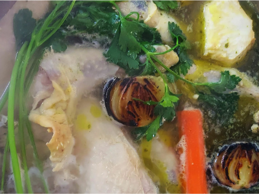 Zbliżenie na gotującą się zupę. W wodzie widać nać pietruszki, marchewkę, opaloną cebulę i ziemniaki.