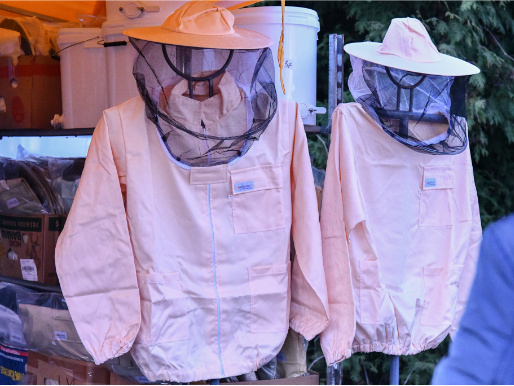 Na wieszaku wiszą dwie kurtki pszczelarskie z kapeluszami z siatką ochronną.