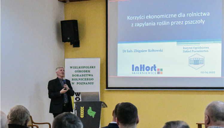 Jednym z wykładowców był profesor Zbigniew Kołtowski z Instytutu Ogrodnictwa, Zakładu Pszczelnictwa w Puławach oraz wiceprezes Polskiego Związku Pszczelarskiego Mężczyzna wygłasza wykład, na ekranie wyświetla się prezentacja multimedialna. Na pierwszym planie widać od tyłu siedzących słuchaczy.