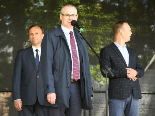 Na scenie stoi trzech mężczyzn. Jeden z nich przemawia.