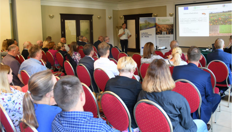 Sala konferencyjna. Od tyłu widać publiczność, przed którą jest ekran z prezentacją.