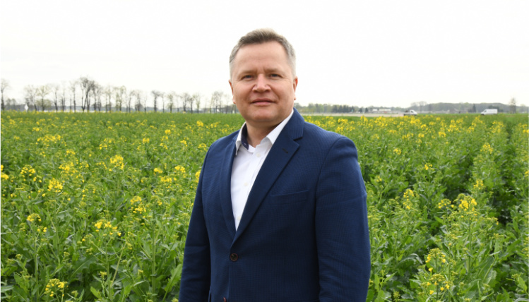 Michał Sosiński stoi wyprostowany na polu w Sielinku. W tle widoczne są uprawy.